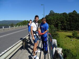 Un hombre con arnés se prepara para una emocionante experiencia de puenting en Pontevedra, en Sinde, asistido por un instructor. Vista del bosque y cielo despejado al fondo. - ForTwo - Planes para parejas