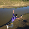 Un atrevido entusiasta se lanza con los brazos extendidos sobre el río Guadiana, luciendo una vibrante camisa y arnés de color morado en la experiencia Puenting ¡Atrévete a Volar sobre el Guadiana!. - ForTwo - Planes para parejas