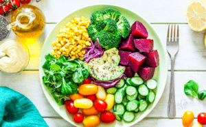 Disfrute de una creación de Taller de Cocina Saludable con esta vibrante ensalada de tomates, pepinos, maíz, brócoli, remolacha, aguacate y verduras presentadas elegantemente en un plato blanco. - ForTwo - Planes para parejas
