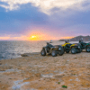 Experimenta la emoción de un "Tour en quad por Ibiza: Aventura y paisajes únicos" con cuatro ATV en un acantilado rocoso al atardecer, con vistas al mar y a una isla lejana bajo un cielo colorido, capturando el vibrante encanto de Ibiza. - ForTwo - Planes para parejas