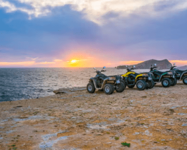 Experimenta la emoción de un "Tour en quad por Ibiza: Aventura y paisajes únicos" con cuatro ATV en un acantilado rocoso al atardecer, con vistas al mar y a una isla lejana bajo un cielo colorido, capturando el vibrante encanto de Ibiza. - ForTwo - Planes para parejas