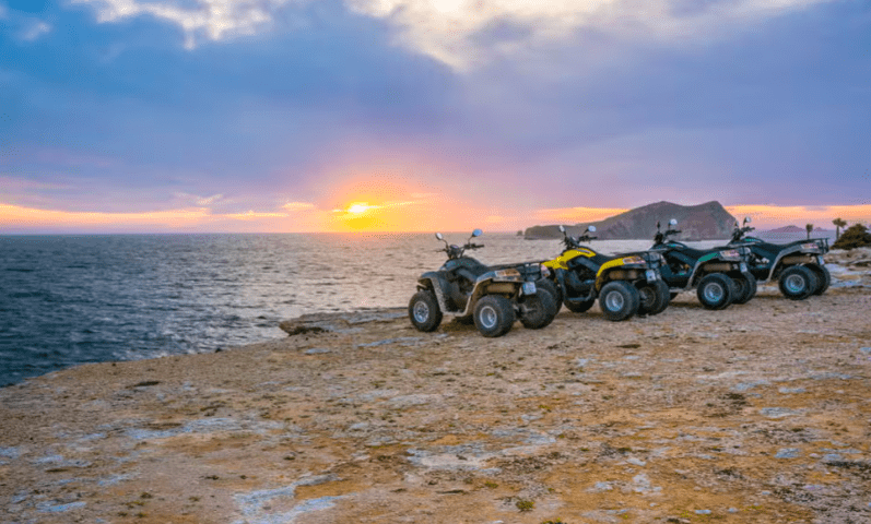 Experimenta la emoción de un "Tour en quad por Ibiza: Aventura y paisajes únicos" con cuatro ATV en un acantilado rocoso al atardecer, con vistas al mar y a una isla lejana bajo un cielo colorido, capturando el vibrante encanto de Ibiza. - ForTwo - Planes para parejas