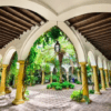 Descubra un tranquilo patio con jardín inspirado en Córdoba en el Palacio de Viana, con senderos arqueados, elegantes columnas, una palmera central y un techo de madera. Este oasis escondido ofrece una tranquilidad similar a la de un tour por el Palacio de Viana. - ForTwo - Planes para parejas