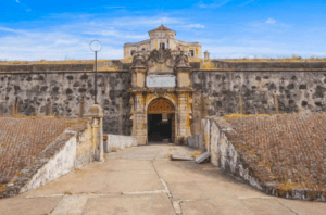 Experimente el "Tour por las murallas de Badajoz y Elvas" y explore una fortaleza histórica con un arco central y muros de piedra que recuerdan a las Murallas de Badajoz. Descubra el camino de entrada bajo un cielo azul que le invita a sumergirse en la rica historia de Elvas. - ForTwo - Planes para parejas