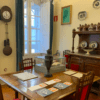 Un comedor vintage con mesa de madera, sillas, reloj y vitrina evoca el ambiente de Visita la Casa-Museo de Picasso. Platos decorativos en las paredes añaden un encanto artístico que recuerda al estilo ecléctico de Picasso. - ForTwo - Planes para parejas