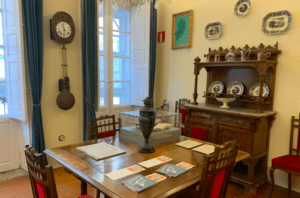 Un comedor vintage con mesa de madera, sillas, reloj y vitrina evoca el ambiente de Visita la Casa-Museo de Picasso. Platos decorativos en las paredes añaden un encanto artístico que recuerda al estilo ecléctico de Picasso. - ForTwo - Planes para parejas