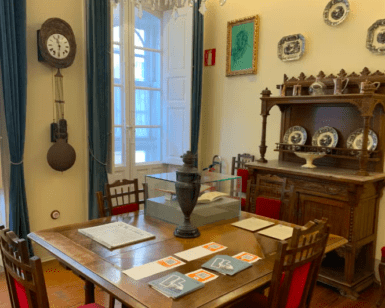 Un comedor vintage con mesa de madera, sillas, reloj y vitrina evoca el ambiente de Visita la Casa-Museo de Picasso. Platos decorativos en las paredes añaden un encanto artístico que recuerda al estilo ecléctico de Picasso. - ForTwo - Planes para parejas