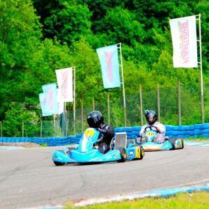 Dos personas compiten en karts a gran velocidad en la emocionante pista Vive la velocidad en el Karting Soto de Dueñas, rodeada de frondosos árboles y vibrantes banderas publicitarias en Asturias. - ForTwo - Planes para parejas