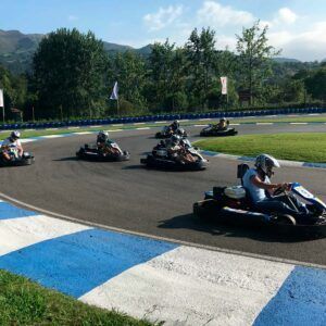 En Karting Soto de Dueñas, Asturias, los competidores compiten con maestría en karts en una pista con bordes azules y blancos, rodeada de frondosos árboles y montañas impresionantes. Experimenta la emoción de "Vive la velocidad". - ForTwo - Planes para parejas