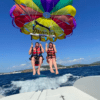 Dos personas disfrutan de una emocionante experiencia de Vuelo en Parasailing en Santa Eulalia del Río, volando alto sobre el océano con un paracaídas vibrante y usando chalecos salvavidas. - ForTwo - Planes para parejas