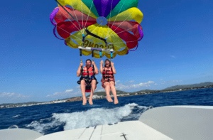Dos personas disfrutan de una emocionante experiencia de Vuelo en Parasailing en Santa Eulalia del Río, volando alto sobre el océano con un paracaídas vibrante y usando chalecos salvavidas. - ForTwo - Planes para parejas