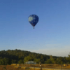 Vuelo en globo: Ibiza desde las alturas al amanecer" ofrece un vuelo sereno en un globo aerostático azul, que se desplaza con gracia sobre el paisaje rural de Ibiza, donde árboles y colinas se despliegan bajo el cielo despejado. - ForTwo - Planes para parejas
