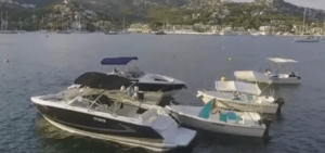 Los barcos sin licencia en Mallorca crean una escena serena mientras se mecen suavemente en una bahía tranquila, recortada contra el fondo de una ciudad montañosa y un puerto deportivo. - ForTwo - Planes para parejas