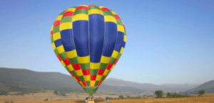 El vibrante globo aerostático a cuadros flota con gracia sobre los campos de hierba cerca de las pintorescas colinas de Reinosa, mostrando la serena belleza de Vuelo en Globo en Reinosa. - ForTwo - Planes para parejas