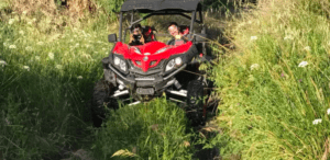 Dos aventureros conducen hábilmente un vehículo todoterreno rojo a través de la hierba alta y el follaje denso, capturando la esencia de una "Aventura Todo Terreno en Badajoz". - ForTwo - Planes para parejas