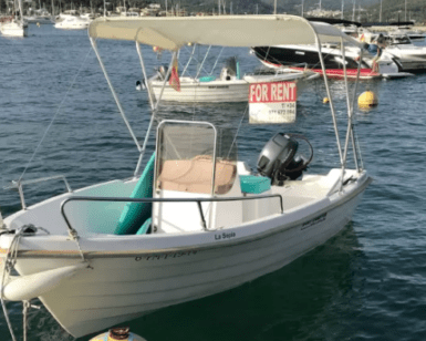 Una pequeña lancha con toldo está fondeada en el puerto de Mallorca, con un cartel de "Se alquila". Es perfecta para quienes buscan "Barco sin licencia en Mallorca", con varias otras embarcaciones visibles al fondo. Ideal para los amantes del alquiler de barcos. - ForTwo - Planes para parejas