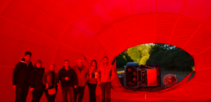 Personas en un globo aerostático rojo preparándose en tierra en Reinosa, rodeadas de árboles y equipo. Es un momento emocionante mientras se preparan para su vuelo en globo en Reinosa. - ForTwo - Planes para parejas