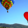 El Vuelo en Globo en Reinosa ofrece una experiencia fascinante con dos globos aerostáticos, uno multicolor y otro rojo, flotando sobre colinas verdes bajo un cielo azul claro. - ForTwo - Planes para parejas