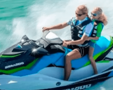 Dos personas surcan las aguas turquesas de Menorca en una "Alquila una Moto de Agua en Menorca", equipadas de forma segura con chalecos salvavidas y gafas de sol. - ForTwo - Planes para parejas