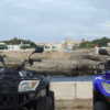 Dos quads aparcados frente al mar ofrecen una vista impresionante de la costa rocosa de Menorca y su encantadora ciudad, ideal para una Aventura en Quad por Menorca. - ForTwo - Planes para parejas