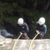 Dos amantes de las emociones fuertes, ataviados con cascos, descienden en rápel por un acantilado junto a una cascada, iniciando una emocionante aventura de Barranquismo de Iniciación en el Valle de Núria. - ForTwo - Planes para parejas