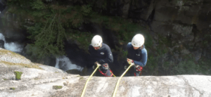 Dos amantes de las emociones fuertes, ataviados con cascos, descienden en rápel por un acantilado junto a una cascada, iniciando una emocionante aventura de Barranquismo de Iniciación en el Valle de Núria. - ForTwo - Planes para parejas