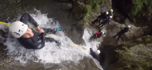 Durante un emocionante Barranquismo de Iniciación en el Valle de Núria, alguien desciende en rápel por una cascada mientras otros observan desde arriba. - ForTwo - Planes para parejas