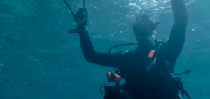 Un buceador experimenta un "Bautismo de Buceo en Mallorca", deslizándose bajo el agua cerca de Mallorca con una máscara y un traje de neopreno, rodeado de burbujas y luz filtrándose a través de la superficie. - ForTwo - Planes para parejas