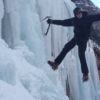 En Sierra Nevada, una persona escala una cascada congelada usando crampones y piolets. Las siluetas de los árboles la envuelven, capturando la emoción del "Bautismo de Escalada en Hielo en Sierra Nevada". - ForTwo - Planes para parejas