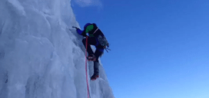 Vestido con equipo de escalada, un aventurero escala un acantilado helado bajo el vasto cielo azul, abrazando la emoción del Bautismo de Escalada en Hielo en Sierra Nevada en medio de majestuosos picos. - ForTwo - Planes para parejas