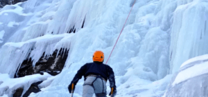 Una persona disfruta de la emoción de escalar en hielo una cascada congelada en Sierra Nevada con Bautismo de Escalada en Hielo, equipada con un casco naranja y confiables herramientas de hielo. - ForTwo - Planes para parejas