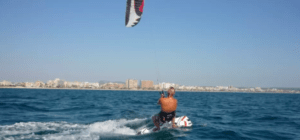 Una persona practicando kitesurf en el océano cerca del impresionante horizonte de Palma de Mallorca bajo un cielo azul claro, disfrutando de la emoción y la aventura de un Bautismo de Kitesurf en Palma de Mallorca. - ForTwo - Planes para parejas