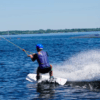 Participando en una Clase Privada de Wakeboard, alguien practica wakeboard con destreza en el lago. Con casco de seguridad, crea un impresionante chapuzón bajo el cielo azul despejado. - ForTwo - Planes para parejas