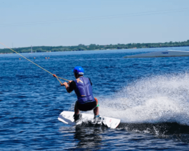 Participando en una Clase Privada de Wakeboard, alguien practica wakeboard con destreza en el lago. Con casco de seguridad, crea un impresionante chapuzón bajo el cielo azul despejado. - ForTwo - Planes para parejas