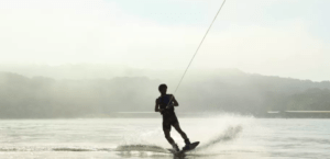 Una silueta de alguien disfrutando de una clase privada de wakeboard en un lago brumoso, enmarcada por majestuosas vistas a las montañas. - ForTwo - Planes para parejas