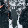 Dos esquiadores vestidos de negro sostienen sus esquís en medio de un bosque nevado de Sierra Nevada durante sus "Clases de Esquí en Sierra Nevada" mientras los copos de nieve caen suavemente a su alrededor. - ForTwo - Planes para parejas