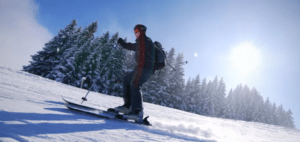 Una persona que toma Clases de Esquí en Sierra Nevada esquía cuesta abajo por una ladera nevada, rodeada de árboles cubiertos de nieve e iluminados por el sol bajo un cielo azul claro. - ForTwo - Planes para parejas