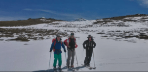 Un trío esquía por una ladera nevada en la impresionante Sierra Nevada bajo un cielo azul claro, tomando "Clases de Esquí en Sierra Nevada". - ForTwo - Planes para parejas