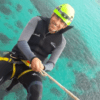 Una persona vestida con traje de neopreno y casco muestra una brillante sonrisa mientras disfruta del Coasteering en Manacor sobre sus cristalinas aguas azules. - ForTwo - Planes para parejas