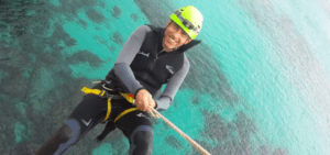 Una persona vestida con traje de neopreno y casco muestra una brillante sonrisa mientras disfruta del Coasteering en Manacor sobre sus cristalinas aguas azules. - ForTwo - Planes para parejas