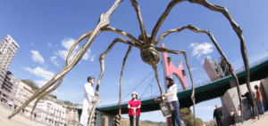 Los visitantes se sitúan bajo una gran escultura de araña junto a un puente contra el cielo azul claro mientras exploran la animada escena artística de Bilbao con "Descubre Bilbao en Segway". - ForTwo - Planes para parejas