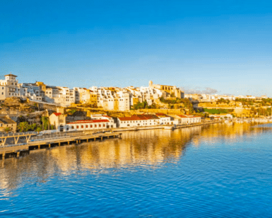 Experimente el pintoresco Mahón con "Descubre Mahón a Tu Ritmo", donde los edificios blancos se funden con un sereno mar azul bajo un cielo despejado, ideal para el turismo. - ForTwo - Planes para parejas