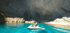 Una persona en un Descubre Mallorca en Moto de Agua navega por las aguas turquesas de una cueva, rodeada de las paredes de roca texturizadas de Mallorca para una escapada inolvidable. - ForTwo - Planes para parejas