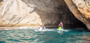 Dos personas en motos de agua 'Descubre Mallorca en Moto de Agua' exploran la entrada de una cueva rocosa en medio de las impresionantes aguas azules de Mallorca. - ForTwo - Planes para parejas