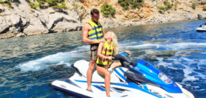 Dos personas con chalecos salvavidas exploran las cristalinas aguas azules cerca de los acantilados rocosos de Mallorca utilizando "Descubre Mallorca en Moto de Agua". - ForTwo - Planes para parejas