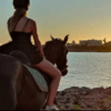 Dos personas cabalgando cerca de una costa rocosa de Menorca, disfrutando de la puesta de sol sobre el agua, mientras experimentan la impresionante belleza de la naturaleza con "Descubre Menorca a Caballo". - ForTwo - Planes para parejas