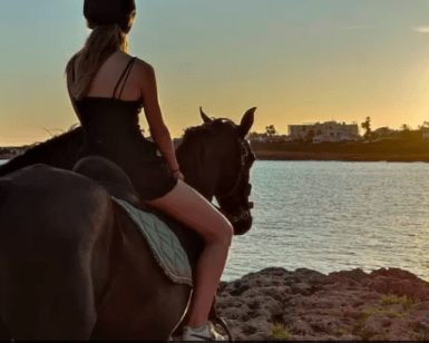 Dos personas cabalgando cerca de una costa rocosa de Menorca, disfrutando de la puesta de sol sobre el agua, mientras experimentan la impresionante belleza de la naturaleza con "Descubre Menorca a Caballo". - ForTwo - Planes para parejas