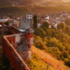 Vista aérea de Hostalric que muestra el Castell d'Hostalric, un encantador castillo de piedra, y su iglesia, rodeados de exuberante vegetación al atardecer. Descubre este pintoresco paisaje donde la historia se fusiona con la belleza natural con Descubre el Castell d'Hostalric. - ForTwo - Planes para parejas