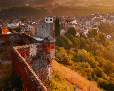 Vista aérea de Hostalric que muestra el Castell d'Hostalric, un encantador castillo de piedra, y su iglesia, rodeados de exuberante vegetación al atardecer. Descubre este pintoresco paisaje donde la historia se fusiona con la belleza natural con Descubre el Castell d'Hostalric. - ForTwo - Planes para parejas
