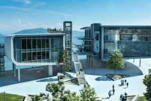 Con vistas al agua, el moderno Centro Botín cuenta con elegantes escaleras llenas de gente. Enmarcado por frondosos árboles y una majestuosa montaña bajo un cielo azul vibrante, Descubre el Centro Botín ofrece una serena fusión de naturaleza e innovación. - ForTwo - Planes para parejas